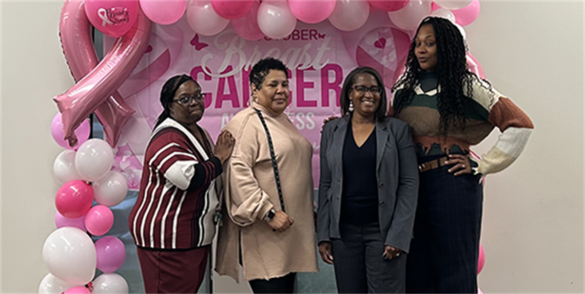 Four ladies in front of pink balloon banner for breast cancer awareness
