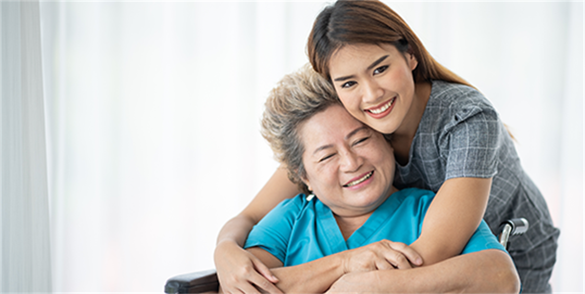 Young Asian woman caregiver hugging an older Asian woman in a wheelchair